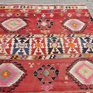 May include: A traditional Turkish rug with a red background and intricate geometric patterns in shades of blue, white, orange, and pink.