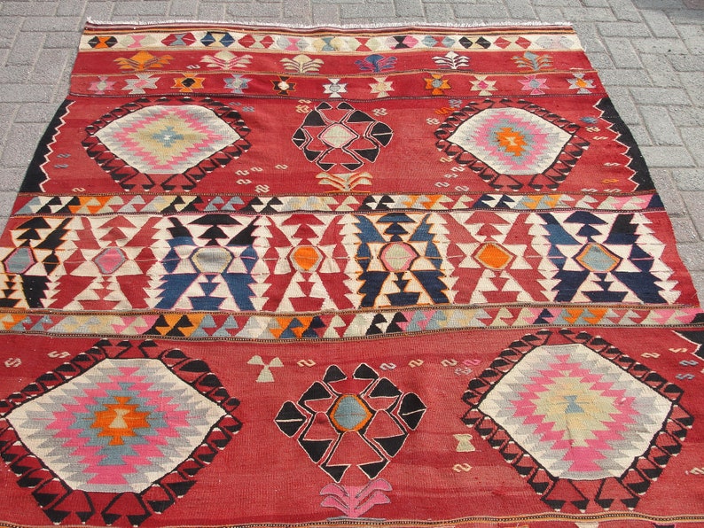 May include: A traditional Turkish rug with a red background and intricate geometric patterns in shades of blue, white, orange, and pink.