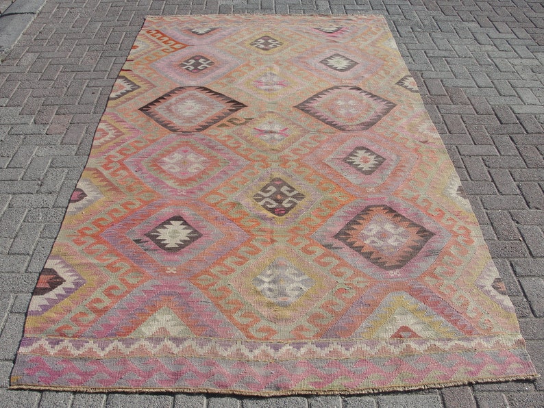 K&ouml;nnte beinhalten: Ein antiker t&uuml;rkischer Teppich mit einem geometrischen Muster in Rosa-, Orange- und Braunt&ouml;nen. Der Teppich hat einen verblassten, abgenutzten Look, der ihm ein rustikales und antikes Aussehen verleiht.