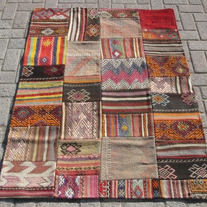 May include: A patchwork rug with a variety of geometric patterns and colors. The rug is made up of rectangular pieces of fabric in shades of red, orange, yellow, green, blue, and brown. The rug is rectangular in shape.
