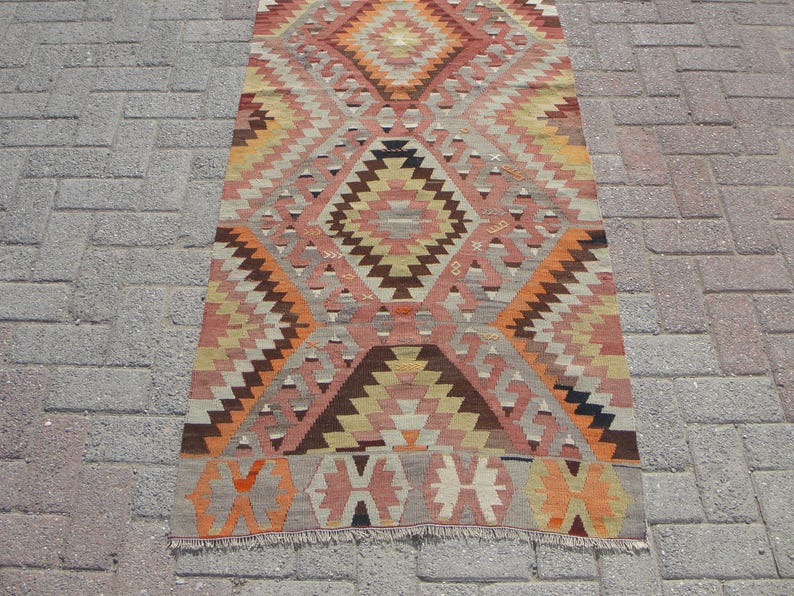 May include: A rectangular, patterned rug with a geometric design. The rug features a central diamond motif in shades of peach, brown, and orange, surrounded by zig-zag and triangular patterns. The rug is approximately 3 feet wide and 6 feet long.