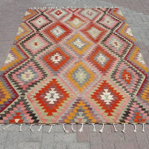 Op de afbeelding: Een traditioneel Turks tapijt met een geometrisch patroon in tinten rood, oranje, roze, geel en grijs. Het tapijt heeft een franje rand.
