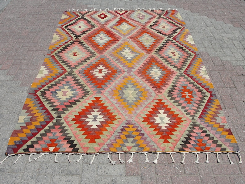 Op de afbeelding: Een traditioneel Turks tapijt met een geometrisch patroon in tinten rood, oranje, roze, geel en grijs. Het tapijt heeft een franje rand.