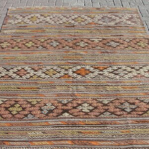K&ouml;nnte beinhalten: Ein rechteckiger, handgewebter Teppich mit geometrischem Muster. Der Teppich weist eine Kombination aus Braun-, Orange-, Beige- und Gelbt&ouml;nen auf. Das Design umfasst horizontale Streifen und rautenf&ouml;rmige Motive.