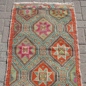 Puede incluir: Una alfombra turca vintage con un patr&oacute;n geom&eacute;trico en tonos de rojo, verde, naranja, rosa y amarillo. La alfombra tiene un borde con flecos y est&aacute; hecha de lana.