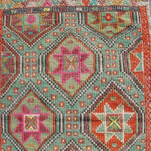 Puede incluir: Una alfombra turca tradicional con un patr&oacute;n geom&eacute;trico en tonos rojos, verdes, naranjas y rosas. La alfombra tiene un borde con flecos y est&aacute; tejida con detalles intrincados.