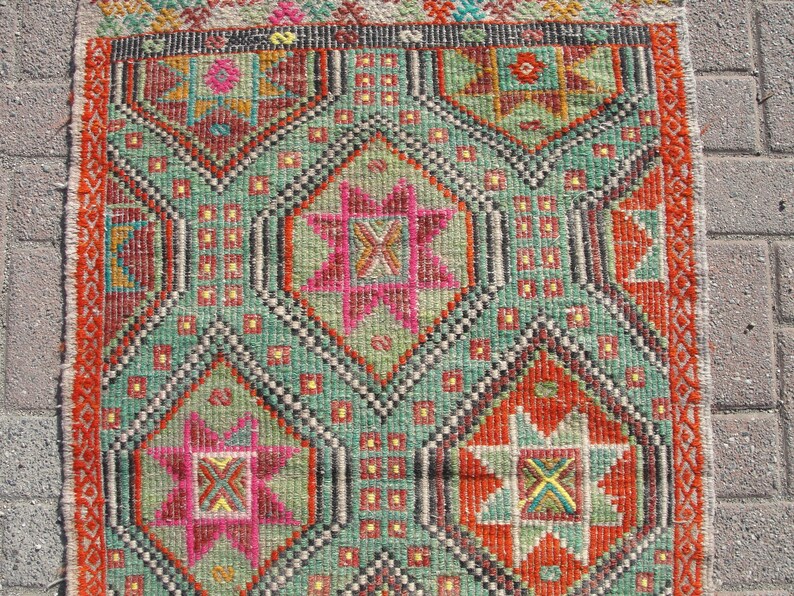 Puede incluir: Una alfombra turca tradicional con un patr&oacute;n geom&eacute;trico en tonos rojos, verdes, naranjas y rosas. La alfombra tiene un borde con flecos y est&aacute; tejida con detalles intrincados.