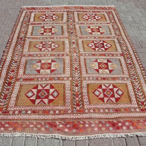 May include: A red, white, and brown patterned rug with a geometric design. The rug has a fringe border.
