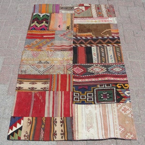 May include: A rectangular patchwork rug with a variety of colorful geometric patterns. The rug features a mix of red, orange, green, and beige sections, creating a vibrant and textured appearance. The design includes stripes, zigzags, and other traditional motifs.