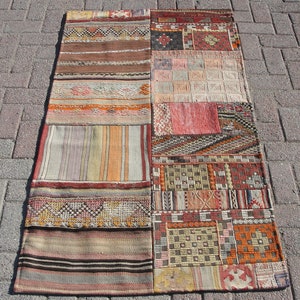 Op de afbeelding: Een patchwork tapijt met verschillende kleuren en patronen, waaronder rood, oranje, bruin en beige. Het tapijt is geweven en heeft een gefranst randje.