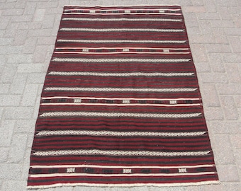 May include: A rectangular rug with a striped pattern in shades of burgundy, black, and white. The rug features horizontal stripes of varying widths, with decorative geometric patterns in white and black.