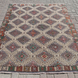 May include: A vintage rug with a geometric pattern in shades of red, green, brown, and white. The rug has a diamond-shaped design with intricate details.