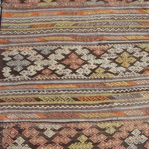 K&ouml;nnte beinhalten: Nahaufnahme eines gewebten Teppichs mit geometrischem Muster. Der Teppich zeigt eine Mischung aus Farben, darunter Braun, Orange, Gelb und Grau. Das Design umfasst Diamanten und Streifen, die ein strukturiertes Aussehen erzeugen. Der Teppich ist wahrscheinlich aus Naturfasern gefertigt.