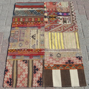 May include: A patchwork rug with a variety of geometric patterns and colors. The rug is made up of rectangular sections with different designs, including stripes, diamonds, and other shapes. The color palette includes red, blue, yellow, and brown.