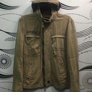 May include: A tan jacket with a hood and a full-length zipper. The jacket has multiple pockets and the word "AVIREX" printed on the chest. Additional text and graphics are printed on the jacket, including "U.S.A. 705978".