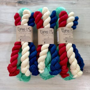 Può includere: Tre matasse di filato tinto a mano, ciascuna avvolta in un'etichetta di carta con la scritta Three by the Sea. Il filato presenta una tavolozza di colori patriottici rosso, bianco e blu, con fili aggiuntivi in verde acqua chiaro.