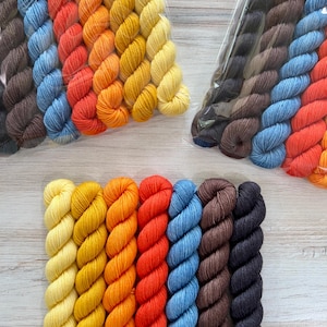 May include: Bundles of colorful yarn in shades of yellow, orange, red, blue, and brown. The yarn is tightly wound and packaged in clear plastic. The arrangement of colors creates a gradient effect, perfect for knitting or crochet projects.
