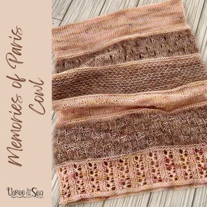 May include: A knitted shawl in shades of peach, brown, and cream with a textured pattern. The shawl is folded and laid on a wooden surface. The text "Memories of Paris Cowl" is visible in the image.