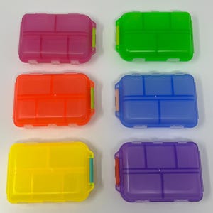 Puede incluir: Seis organizadores de pastillas de pl&aacute;stico transl&uacute;cido de colores brillantes: rosa, verde, naranja, azul, amarillo y morado. Cada caja rectangular tiene una tapa con bisagras y m&uacute;ltiples compartimentos internos para organizar medicamentos o art&iacute;culos peque&ntilde;os.