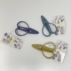 Pode incluir: Três pares de mini tesouras em roxo, azul e dourado. Cada par tem uma alça curva e uma lâmina pontiaguda. As tesouras têm uma etiqueta que diz "Super Snips mini".