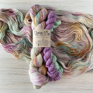 以下が含まれることがあります： 紫、緑、ベージュなど、さまざまな色の手染め糸。ラベルには「Three by the Sea」と「Made in Sunny Florida」と記載されています。編み物や編み物プロジェクトに最適です。