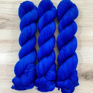 May include: Three skeins of vibrant blue yarn are arranged side by side. The yarn is tightly twisted, revealing a textured surface. The bright blue color is consistent across all three skeins, suggesting a uniform dye lot. The yarn is likely for knitting or crocheting.