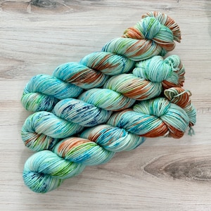 May include: A skein of hand-dyed yarn in shades of blue, green, and brown. The yarn is twisted into a skein, with the colors blending together. The yarn is likely made of wool or a similar fiber, and is suitable for knitting or crocheting.