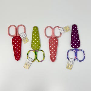 Puede incluir: Cuatro pares de tijeras de bordar con varios diseños de mango. Las tijeras tienen mangos rosas y se combinan con fundas de lunares rojos, rosas, verdes y morados. Cada par tiene una pequeña etiqueta.