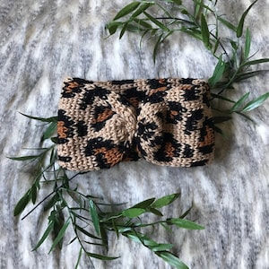 May include: A brown and black leopard print crocheted headband with a knotted design.