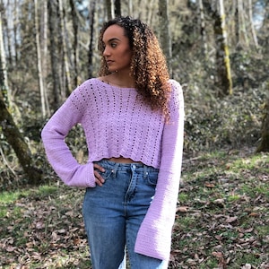 May include: A lavender crocheted cropped sweater with long sleeves. The sweater has a delicate openwork pattern and a scalloped hem.