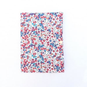 Peut inclure: Une couverture de carnet rectangulaire avec un motif floral. Le fond blanc est orné d'un motif répété de fleurs rouges, bleues et violettes et de feuilles vertes. Une fermeture à bouton-pression dorée est visible sur le côté droit.