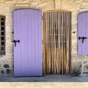 Może przedstawiać: Drzwi drewniane w kolorze fioletowym z czarnym zamkiem i plecioną zasłoną z trawy.