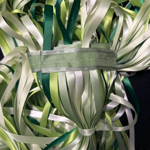 Op de afbeelding: Een bundel groene, witte en crèmekleurige satijnen lint. Het lint is gebonden met een groen lint.