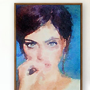 May include: A watercolour portrait of a person with dark hair and intense eyes, framed in a wooden frame. The artwork features a blue and peach colour palette, with the subject's face as the focal point. The painting has a soft, artistic style.