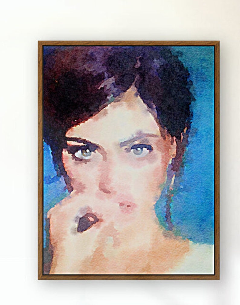 May include: A watercolour portrait of a person with dark hair and intense eyes, framed in a wooden frame. The artwork features a blue and peach colour palette, with the subject's face as the focal point. The painting has a soft, artistic style.