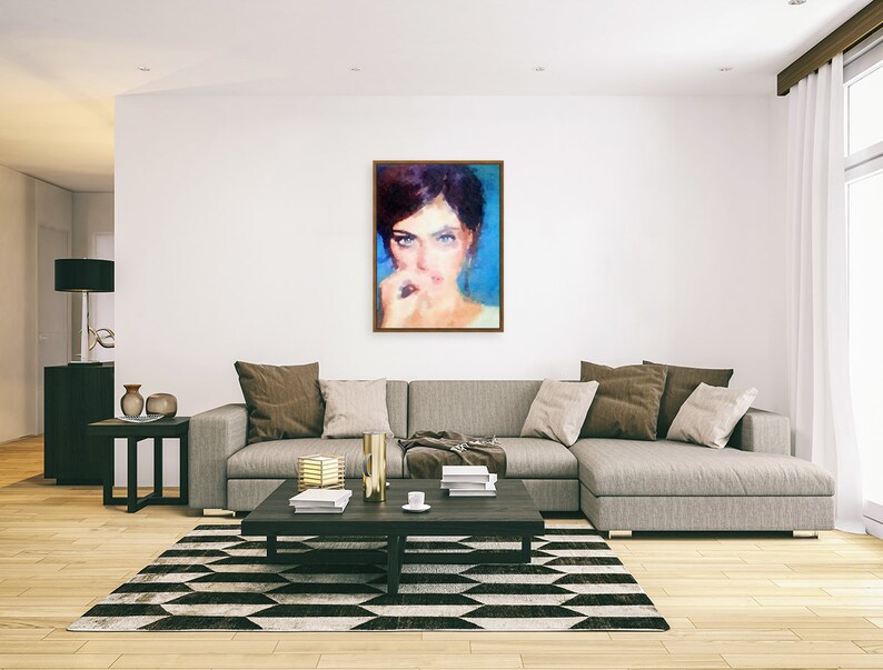 May include: A framed portrait of a woman with dark hair and blue eyes. The painting has a soft, impressionistic style with a blue and beige colour palette. The artwork hangs on a white wall above a grey sectional sofa in a modern living room.