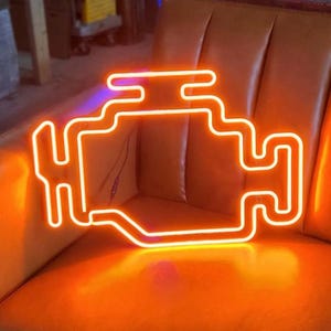 Może przedstawiać: Pomarańczowy neonowy znak w kształcie kontrolki silnika samochodu. Znak jest podświetlony i świeci jasno.