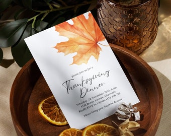 May include: A white card with a handwritten invitation to a Thanksgiving dinner. The card features a watercolor illustration of an orange and yellow maple leaf. The text on the card reads "Please join us for a Thanksgiving Dinner, Saturday, 20 November 2021, 6 pm, 4732 Roame Avenue, Charlotte, Kindly RSVP to Lilyana +123 456 789, Please bring your favorite dessert."