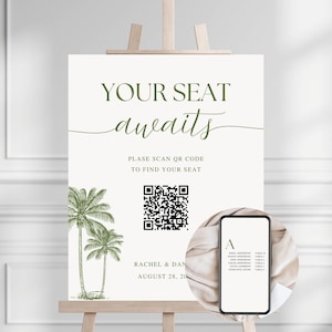 May include: A wedding seating chart sign on an easel. The sign reads "YOUR SEAT awaits" in green script. Below is a QR code and the text "PLEASE SCAN QR CODE TO FIND YOUR SEAT". A smartphone displays a table seating list.