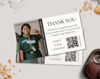 May include: A white thank you card with a black border and text that reads "Thank you. Thanks for supporting our Girl Scout cookie sale! Your purchase makes a big difference. Enjoy your cookies!" There is a black and white QR code on the card. The card has a photo of a young girl wearing a green Girl Scout uniform.
