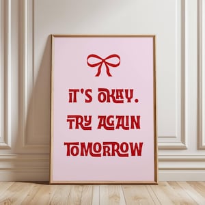 Könnte beinhalten: Ein rosa Poster mit einer roten Schleife und dem Text "Es ist okay. Versuche es morgen nochmal."