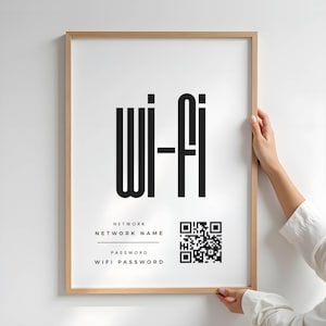 Puede incluir: Impresión enmarcada con la palabra "Wi-Fi" en letras negras en negrita. Debajo, dice "Nombre de la red" y "Contraseña WiFi" con un código QR. El marco es de color marrón claro.
