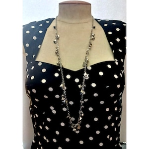 Puede incluir: Un collar de cadena plateada con colgantes geométricos plateados. El collar está en un maniquí de vestido de lunares blancos y negros.