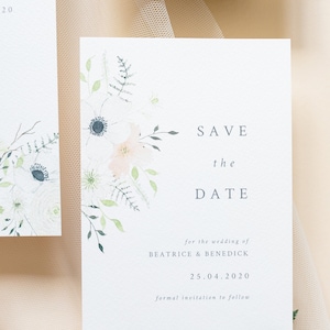 Wedding stationery flat lay with A6 portrait save the date card. Design features spring watercolour florals in peach, white and cream with anemone and ranunculus. Minimal design with elegant serif font printed on luxury white textured card stock.