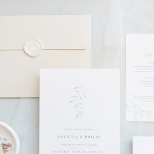 Wedding stationery flat lay with 5x7 invitation, A6 details card, stone envelope and white wax seal. Minimal design with watercolour eucalyptus branch at top with minimal text below in grey, classic serif font. Printed on luxury white textured paper