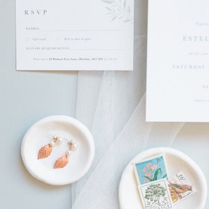 Wedding stationery flat lay with A7 rsvp card and part of 5x7 invitation. Design features minimal watercolour eucalyptus in pale green. Text is all in a classic serif font printed in grey on luxury white textured paper.