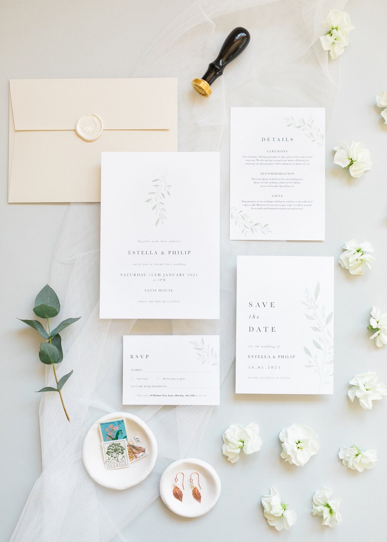 Wedding stationery suite flat lay with 5x7 invitation, A6 save the date, details card, A7 rsvp card, neutral envelope with white wax seal. Minimal watercolour foliage design in pale green. Modern serif font for all text in grey. Printed on luxe paper