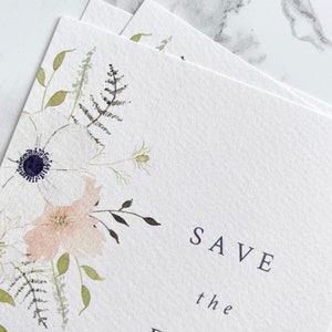 Close up of illustration on A6 save the date card. Watercolour floral illustration with white anemone and peach and cream flowers. Save the date is in aligned right in a minimal, modern style. Printed on luxury white paper.