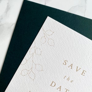 Close up of illustration detail on top corner of wedding save the date card with dark green coloured envelope. Hand drawn honesty branches in delicate line drawing style with save the date in clean and modern serif font in the centre.