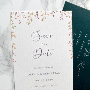Wedding save the date with dark green envelope addressed in silver calligraphy. Autumn design with watercolour leaves coming down from top of the card to frame the text. Save the date is in modern calligraphy with serif text below.